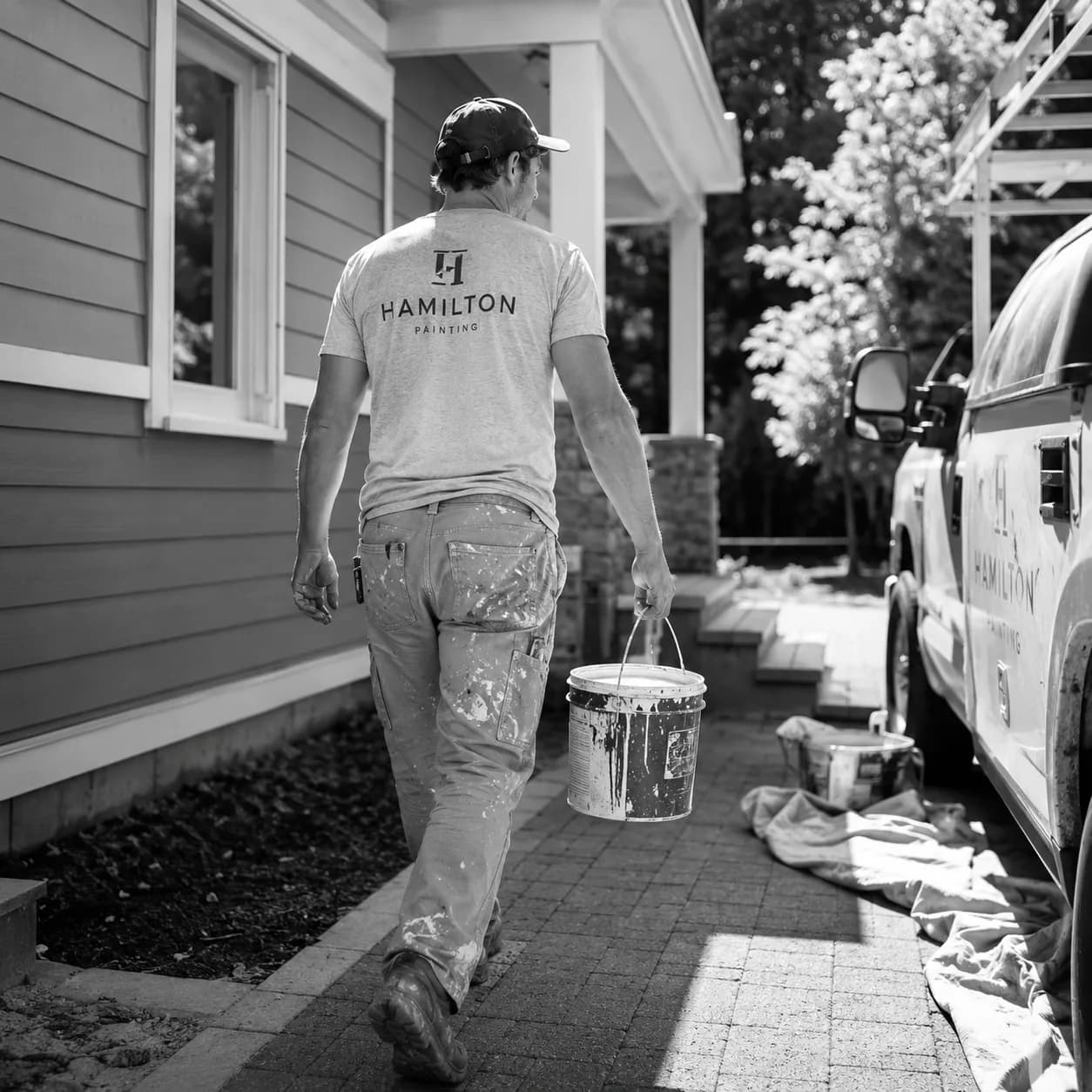 Painter carrying a paint bucket to a job site beside the company truck